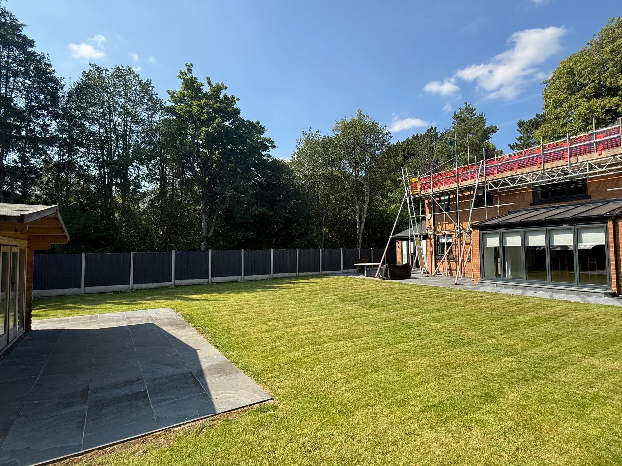 A broad mown lawn running back to mature trees, with a paved sitting area in the foreground