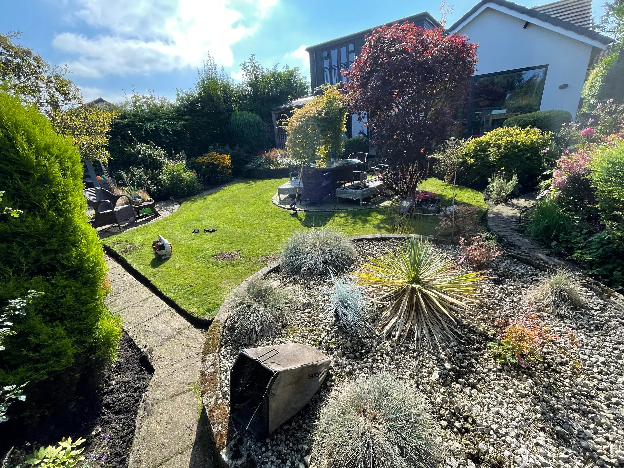 A kept back garden with a mown lawn, a gravel bed of ornamental grasses and a seating area by the house
